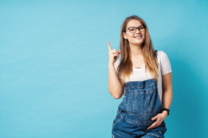 Pretty young pregnant woman pointing with the index finger up a great idea over blue background
