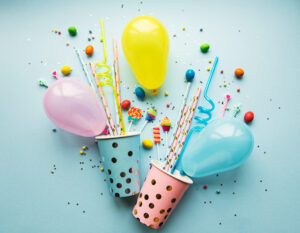 Geburtstagsmotive auf blauem Hintergrund: Partyhütchen, Papierstrohhalme, Süßigkeiten und Luftballons
