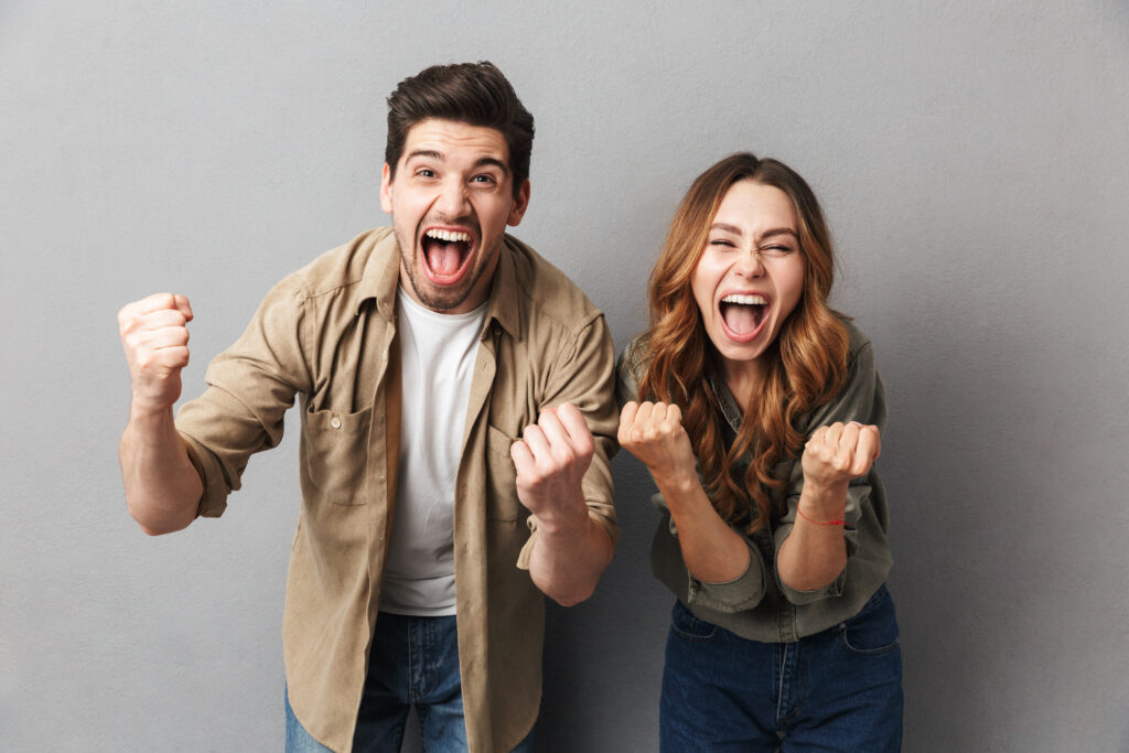 Portrait of a cheerful young couple screaming and celebrating success isolated over gray background