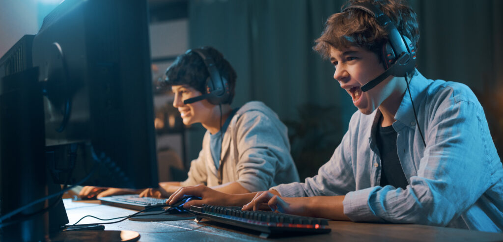Young gamers sitting at desk and playing online video games together, one is shouting into the microphone